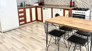 A modern kitchen with wooden cabinets, a white refrigerator, a dishwasher, a washing machine, a stove, and a dining table with chairs.