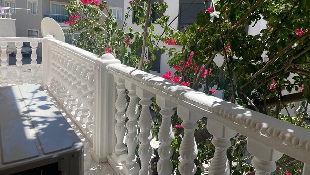 A balcony with a white balustrade and pink flowers.