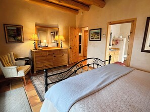 A bedroom with a bed, wooden dresser, chair, and a bathroom visible through an open door.