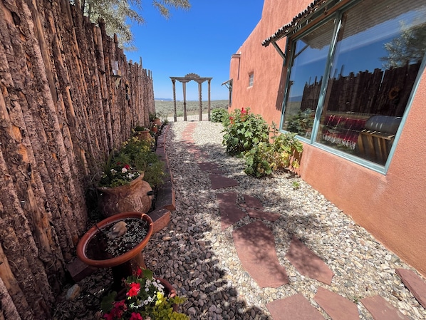 A garden pathway with a rustic fence, potted plants, and a pergola.
