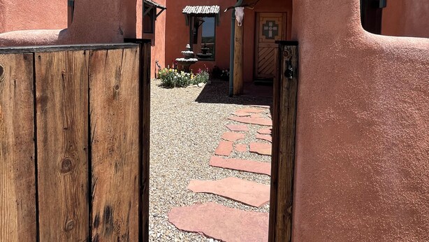 Un arc en pierre rustique mène à une cour intérieure, où l’on trouve un chemin pavé et un bâtiment à l’architecture traditionnelle.