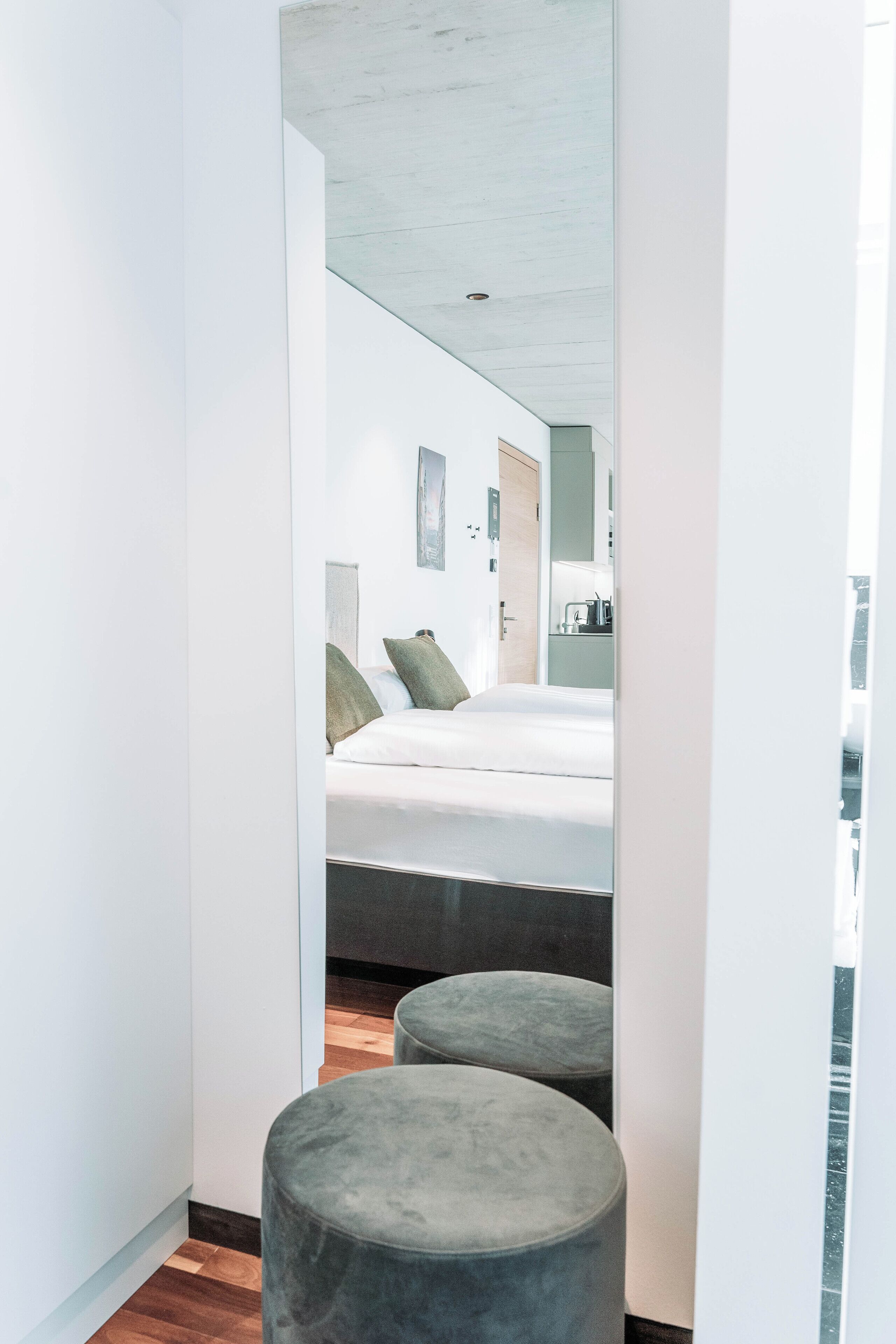 A narrow hallway leading to a bedroom with a bed, a mirror, and a small seating area.