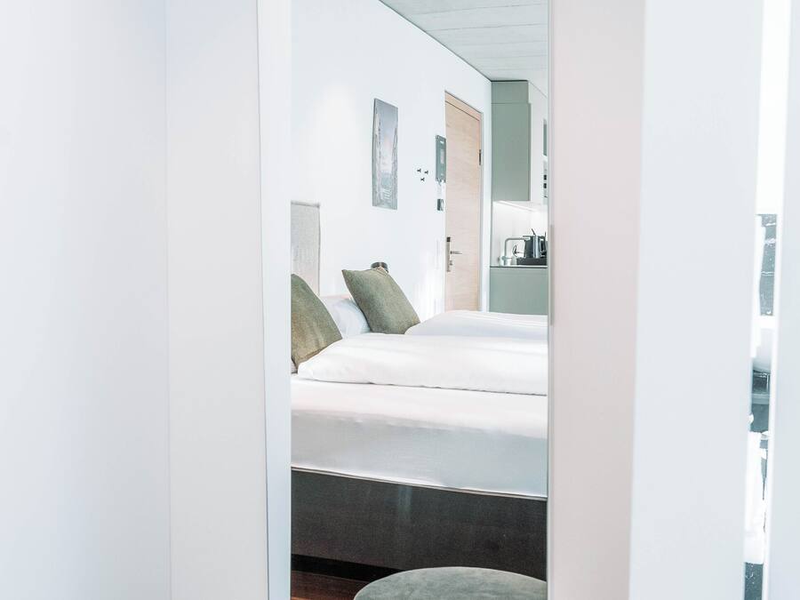 A narrow hallway leading to a bedroom with a bed, a mirror, and a small seating area.
