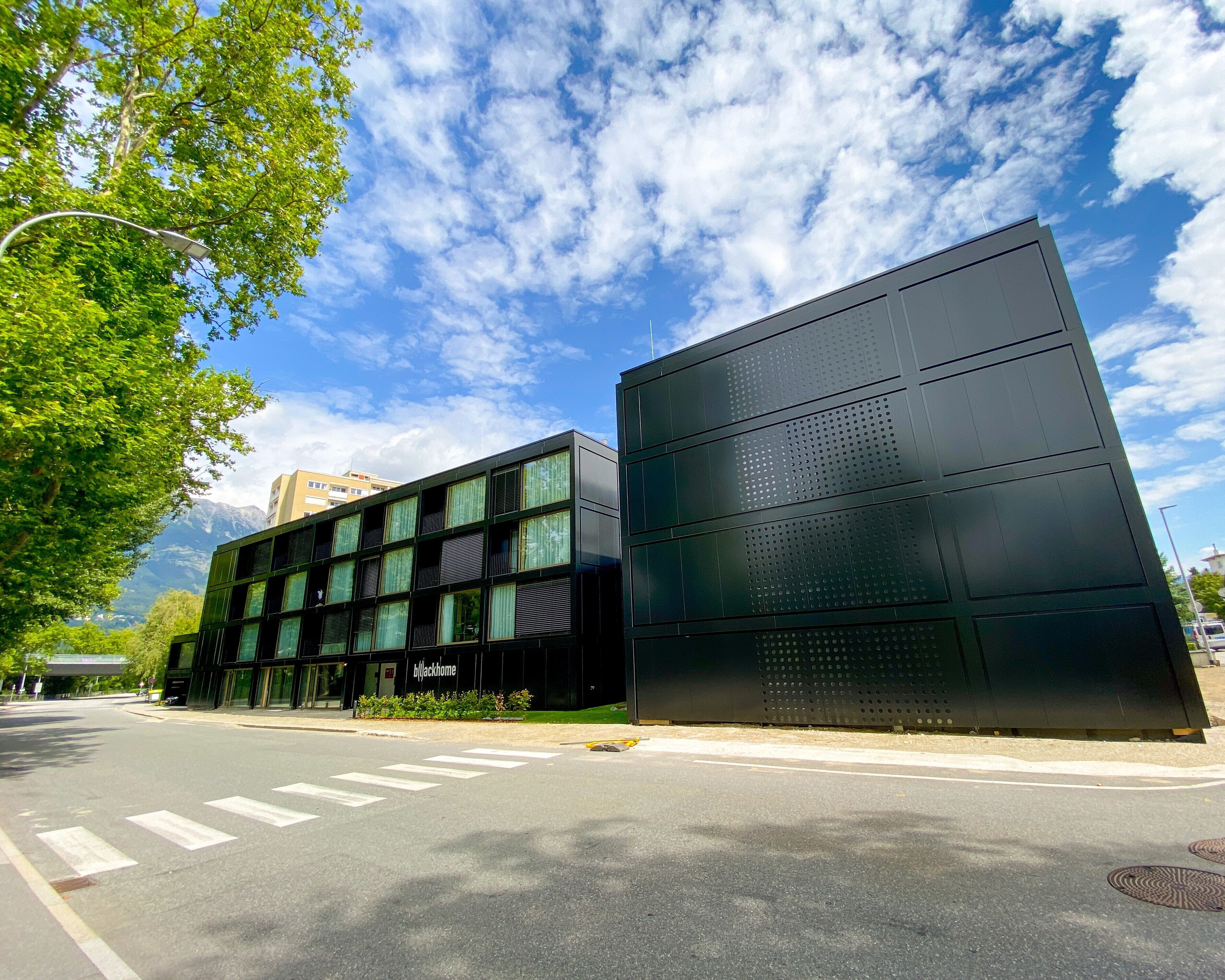 Un edificio moderno con grandes ventanales y fachada plana, situado junto a una calle con paso de peatones.