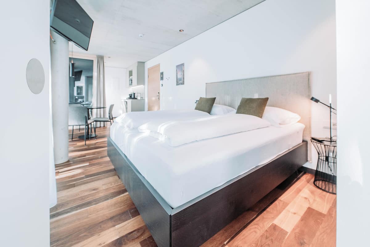 Ein modernes Hotelzimmer mit einem großen Bett, Holzböden, einem Schreibtisch und einer Küchenzeile.