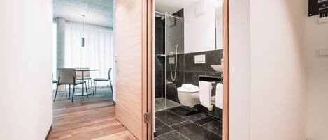 A modern hotel room with a wooden floor, a glass shower, and a white toilet.