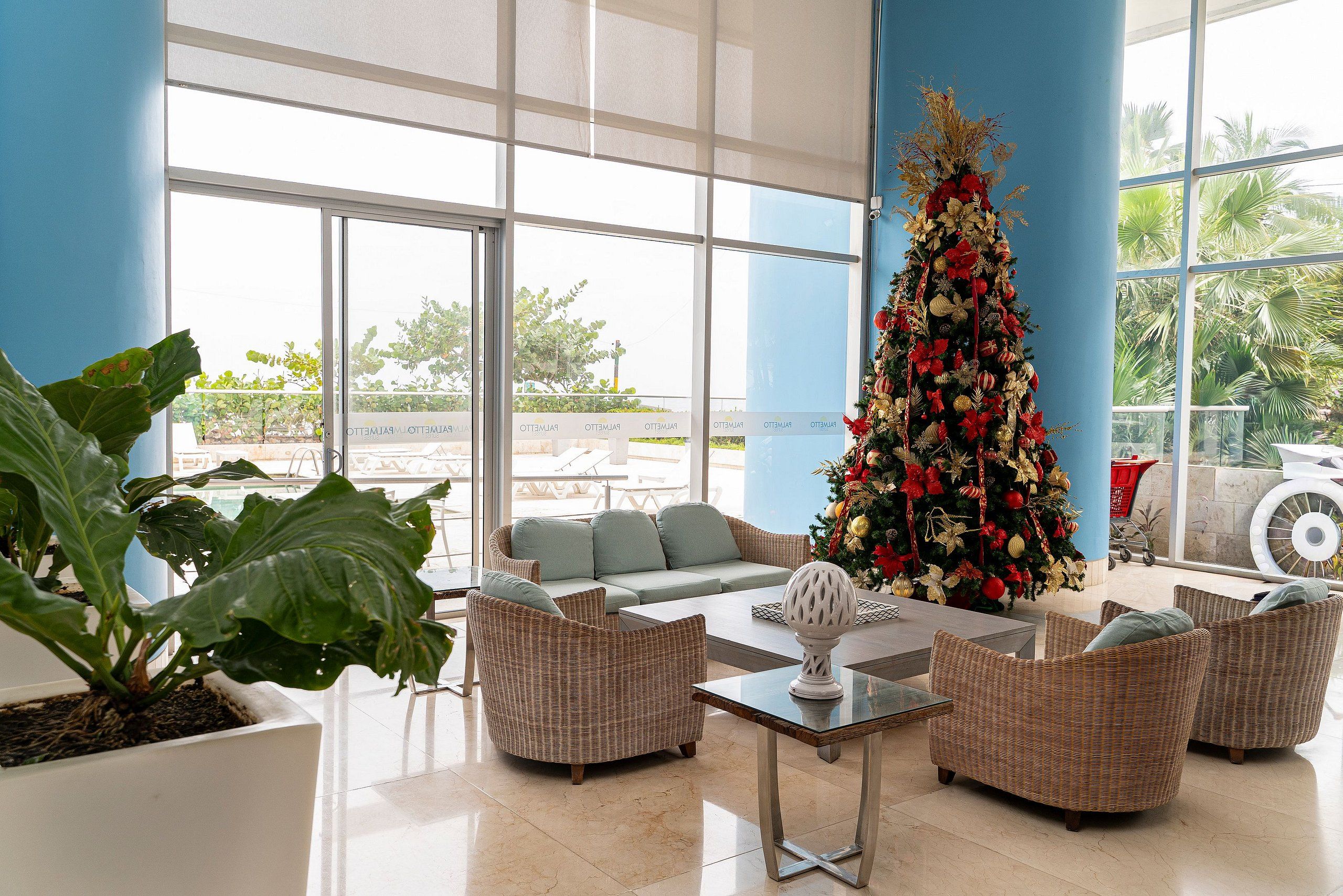 Eine geräumige Lobby mit einem großen Weihnachtsbaum, bequemen Sitzgelegenheiten und Blick auf Palmen durch große Fenster.