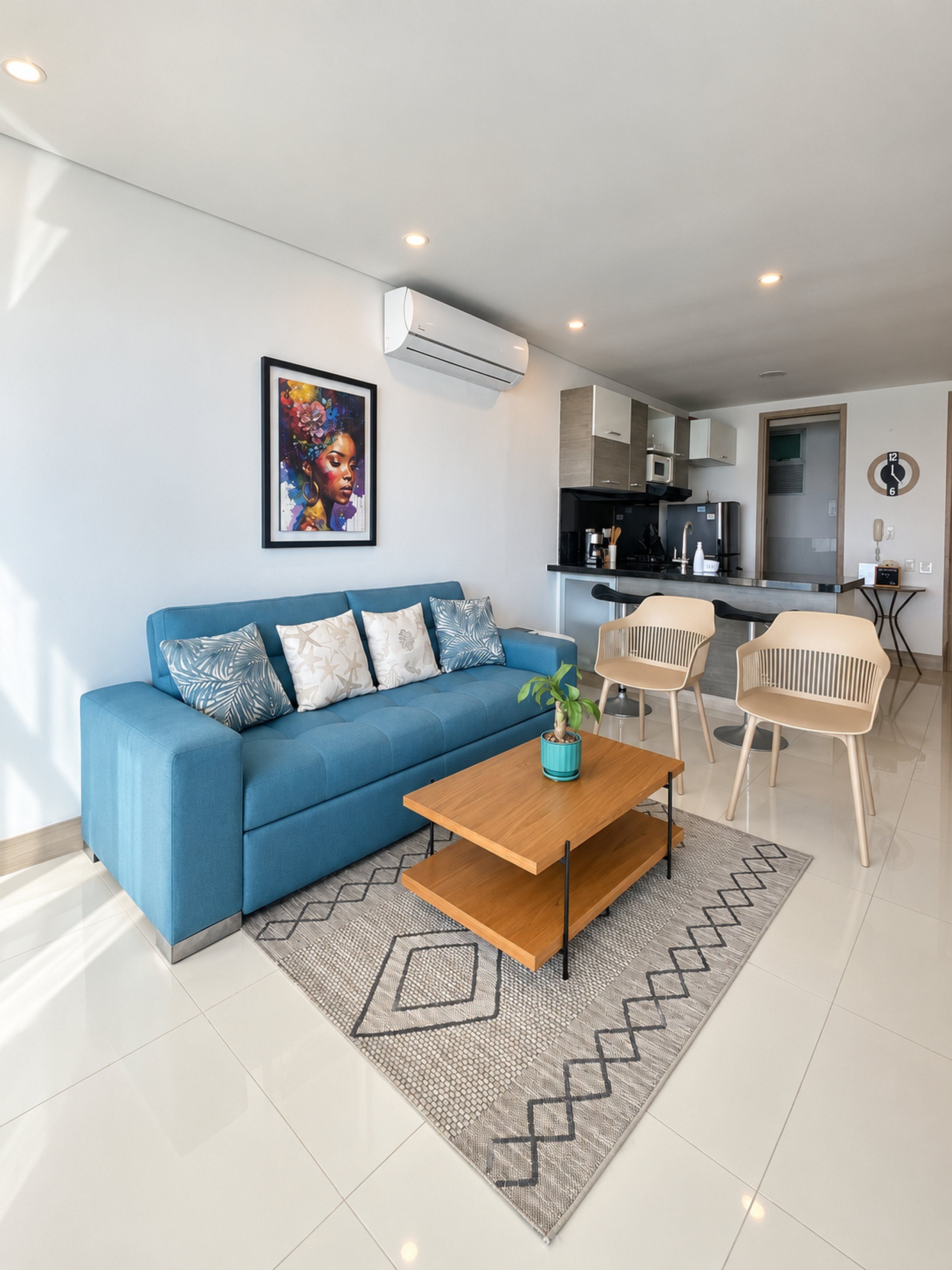 A modern living room with a blue sofa, a wooden coffee table, and a kitchen area in the background.