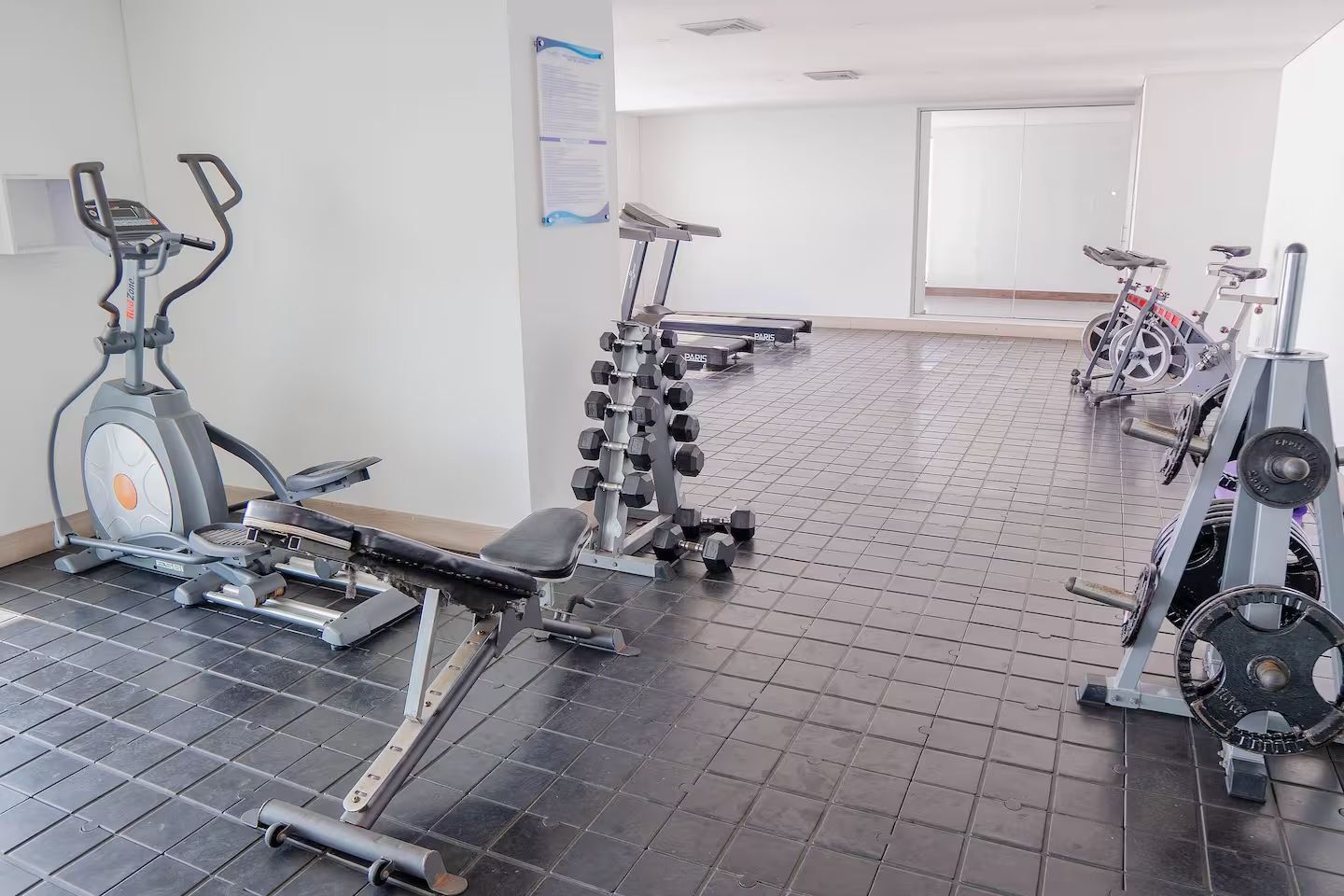 Un gimnasio con equipo de ejercicio, incluyendo cintas de correr, bicicletas estáticas y máquinas de pesas.