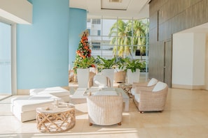 Een moderne zithoek met witte banken, rieten fauteuils en een decoratieve plantenarrangement.