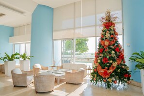 Un vestíbulo espacioso con mobiliario de mimbre, ventanas amplias y un árbol de Navidad decorado.