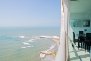 Un balcón con vista al océano, un comedor con sillas y una mesa, y un interior moderno con un espejo grande.