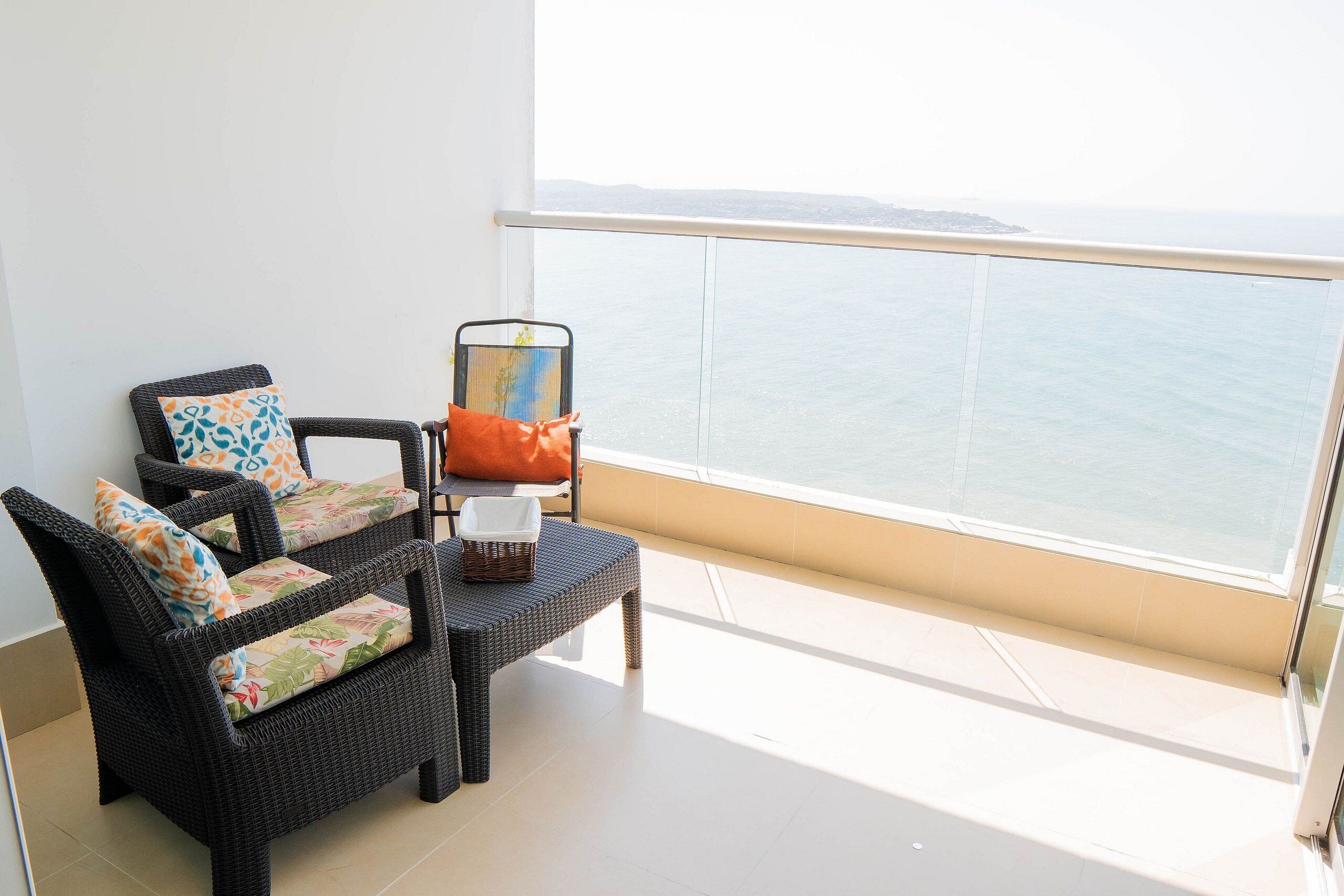 A balcony with wicker furniture, a chair with a cushion, and a view of the sea.