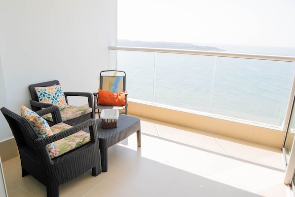 A balcony with wicker furniture, a chair with a cushion, and a view of the sea. - U-GO Palmetto Sunset Junto al Mar (Cartagena)