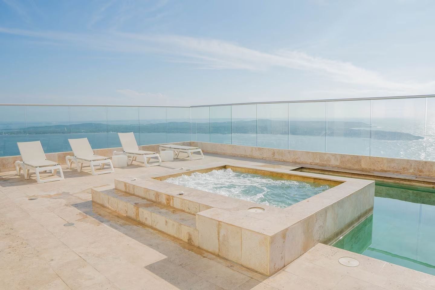 A rooftop infinity pool with a hot tub and lounge chairs, overlooking a scenic view.