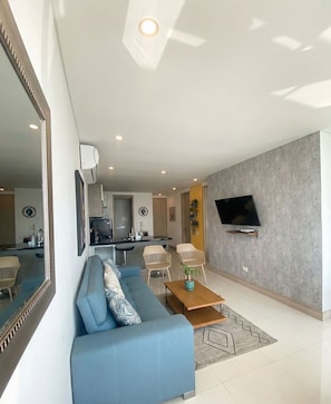 A modern living room with a blue sofa, a coffee table, and a TV mounted on the wall. - U-GO Palmetto Sunset Junto al Mar (Cartagena)