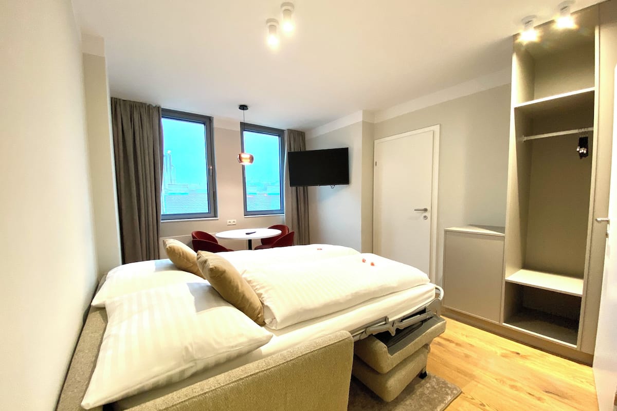 Habitación de hotel con cama, escritorio, silla, televisor y armario.