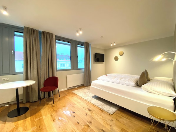 A modern hotel room with a bed, a small table, a red chair, and large windows. - Blackhome Wien (Vienna)