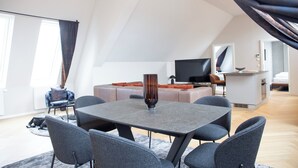 A modern living room with a dining area, a sofa set, a flat-screen TV, and a kitchen area. - Blackhome Wien (Vienna)