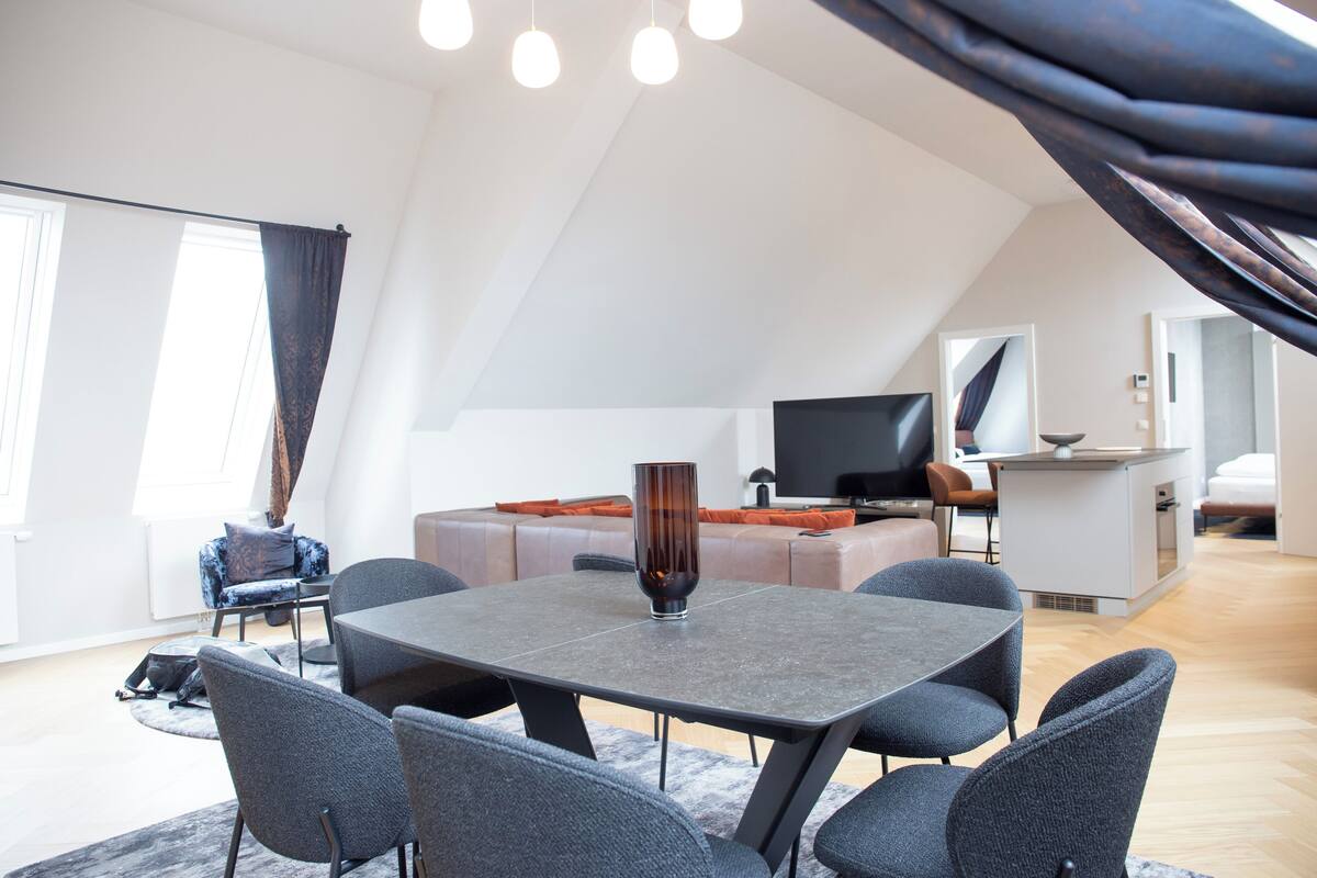 Una sala de estar moderna con comedor, un conjunto de sofás, un televisor de pantalla plana y una cocina.