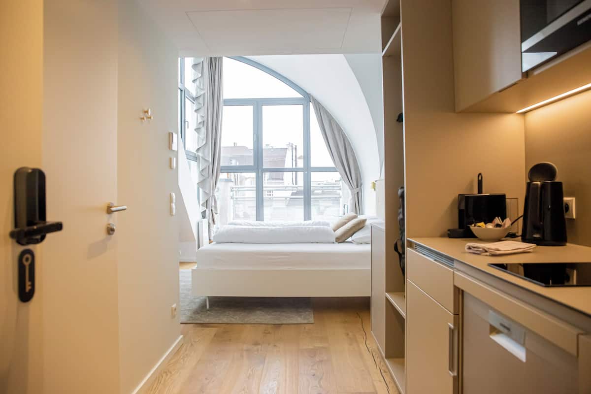 Habitación de hotel compacta con cama, kitchenette y un amplio ventanal con vistas a la ciudad.