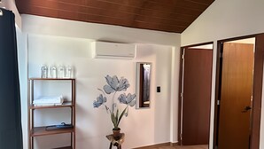 A hotel room with a wooden floor, a shelf with toiletries, a wall-mounted mirror, and a door.