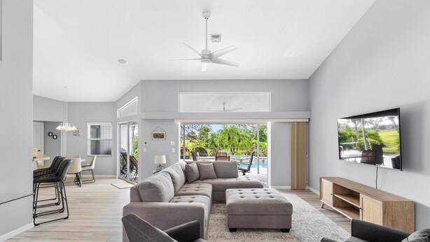 A modern living room with a sectional sofa, a flat-screen TV, and a ceiling fan. - Hello Summer, full refund*, pool heat, sleeps 6 (Rotonda West)