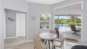 A modern room with a round table and chairs, a hanging light fixture, a door, and a view of an outdoor swimming pool through large glass doors. - Hello Summer, full refund*, pool heat, sleeps 6 (Rotonda West)