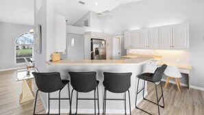 A modern kitchen with a central island, bar stools, and a dining area with a table and chairs. - Hello Summer, full refund*, pool heat, sleeps 6 (Rotonda West)