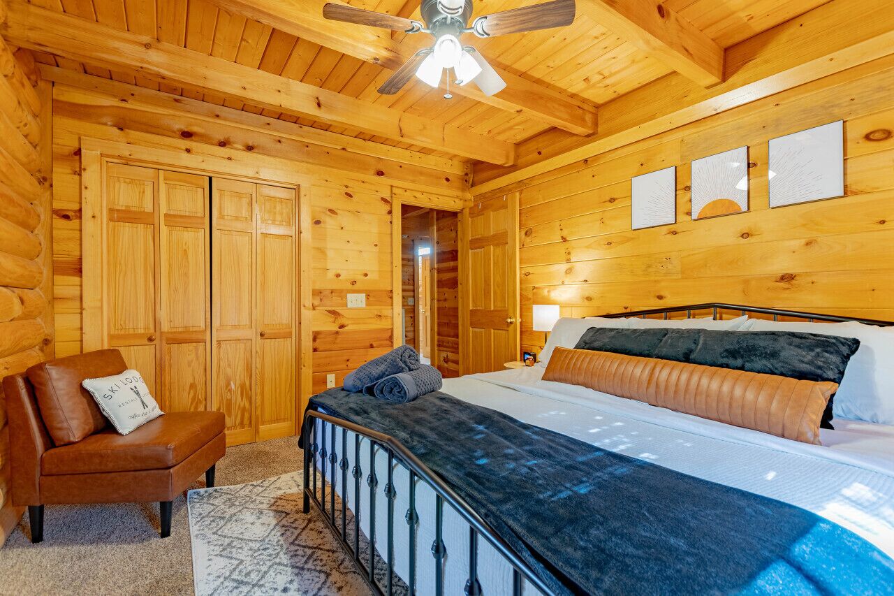 Une chambre dans une cabane en bois, avec un lit, une chaise et un ventilateur de plafond.