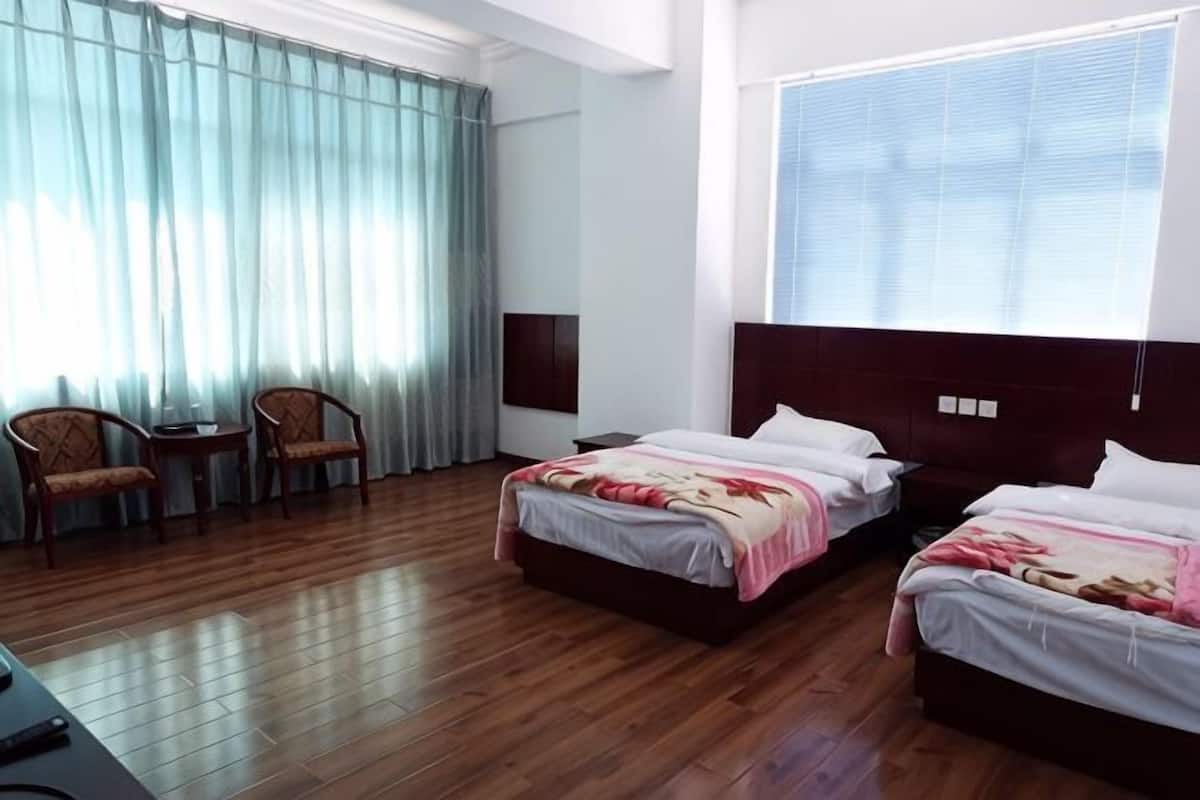 A hotel room with two beds, a desk, chairs, and a large window with curtains.