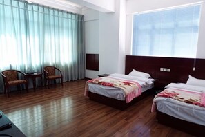 A hotel room with two beds, a desk, chairs, and a large window with curtains.