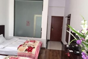 A hotel room with a bed, a desk with a computer, a mirror, and a door.