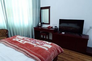 A hotel room with a bed, a desk with a TV, a mirror, and a chair. - Yiyuan Hotel (Yongsheng)