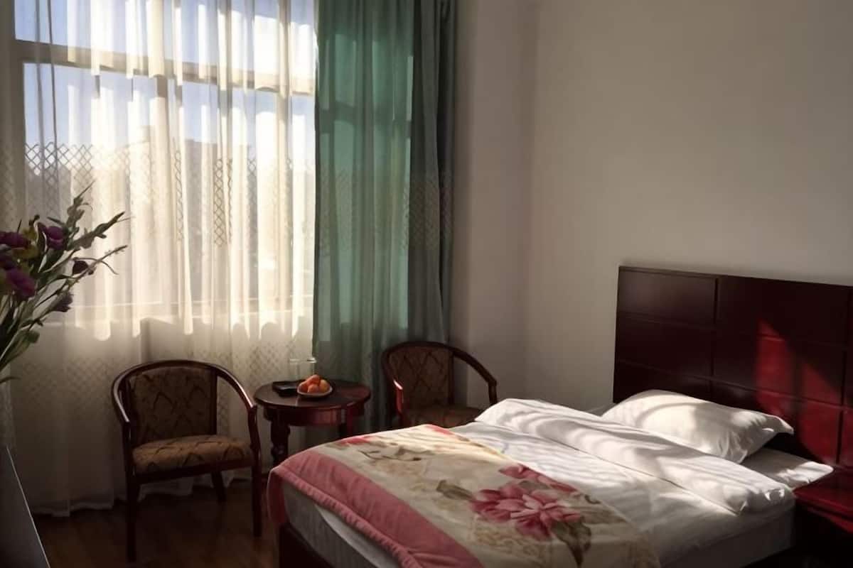 A hotel room with a bed, two chairs, a small table, and a vase of flowers.