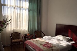 A hotel room with a bed, two chairs, a small table, and a vase of flowers.