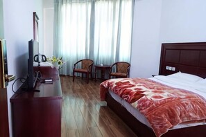 A hotel room with a bed, a desk with a television, two chairs, and a window with curtains. - Yiyuan Hotel (Yongsheng)