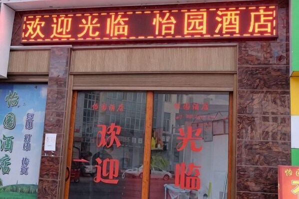 A hotel entrance with a large glass door, a neon sign above, and a stone facade. - Yiyuan Hotel (Yongsheng)