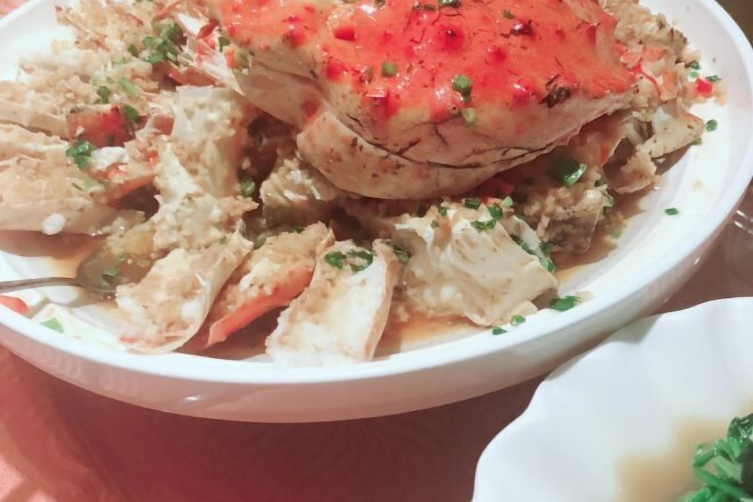 A bowl of crab with a red topping, garnished with herbs.