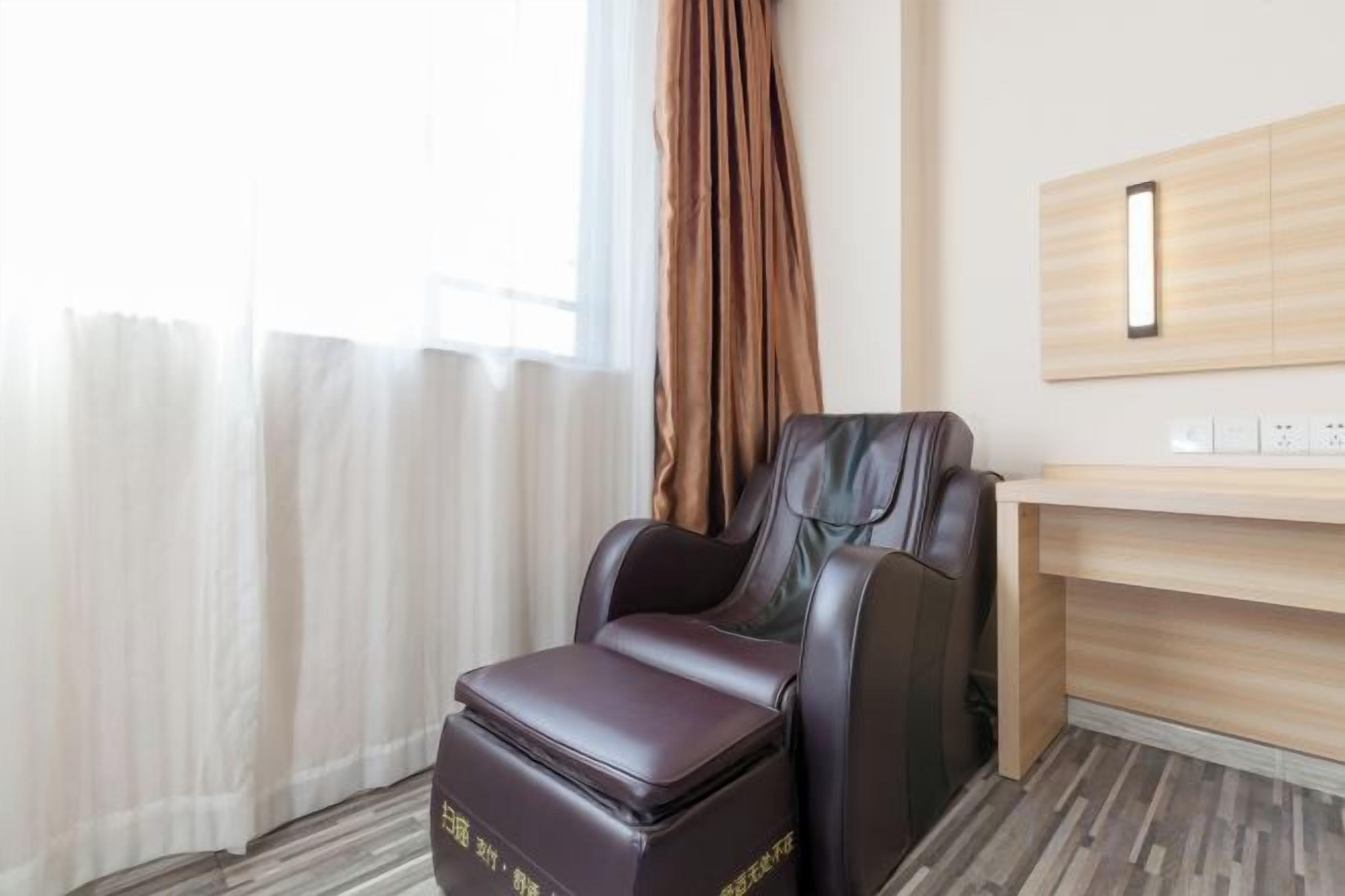 Un fauteuil de massage dans une chambre d’hôtel, avec un bureau en bois et un miroir.