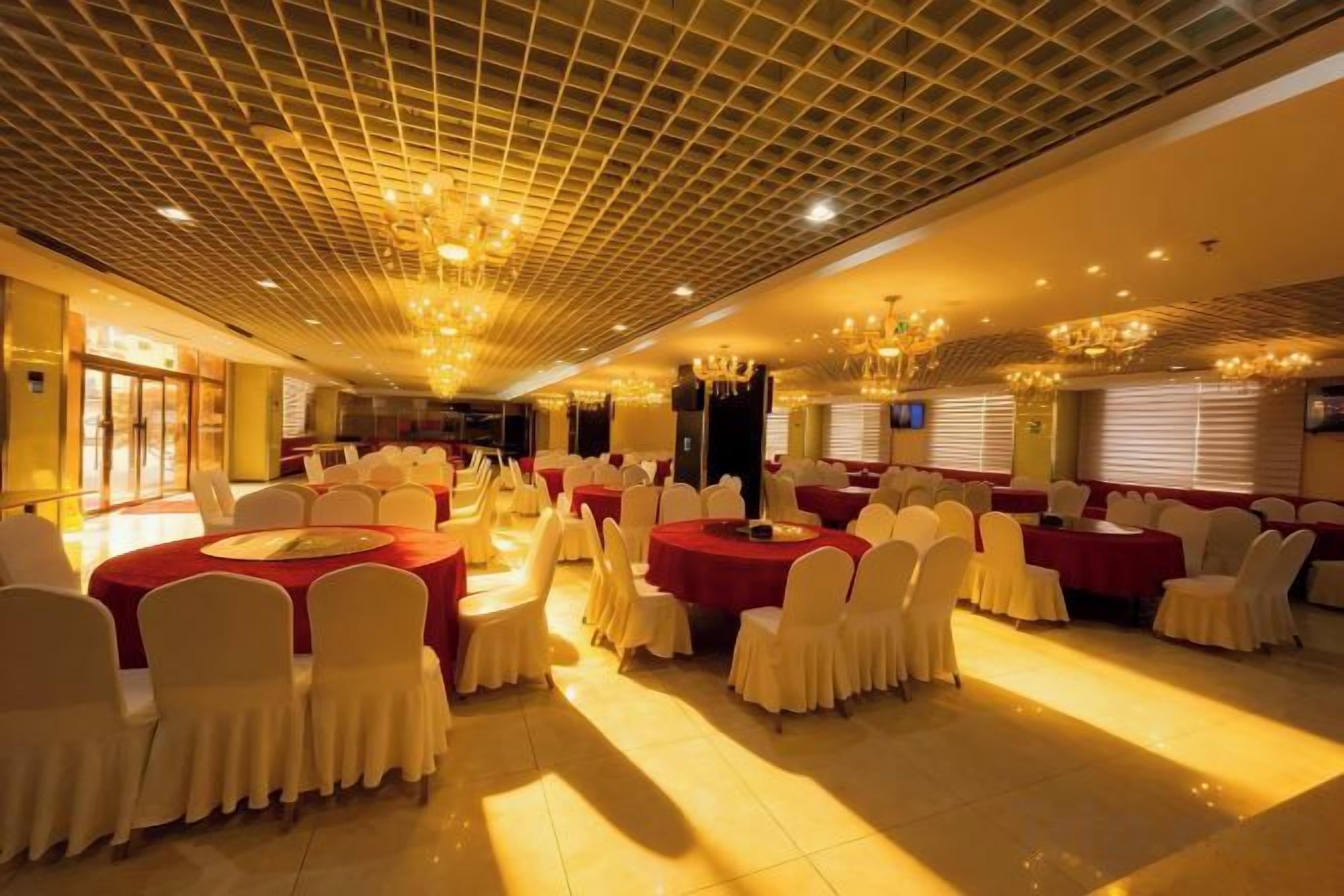 Une salle de banquet avec des tables rondes, des chaises blanches et des nappes rouges.