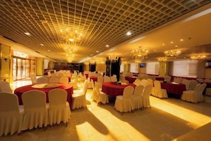 A banquet hall with round tables, white chairs, and red tablecloths.