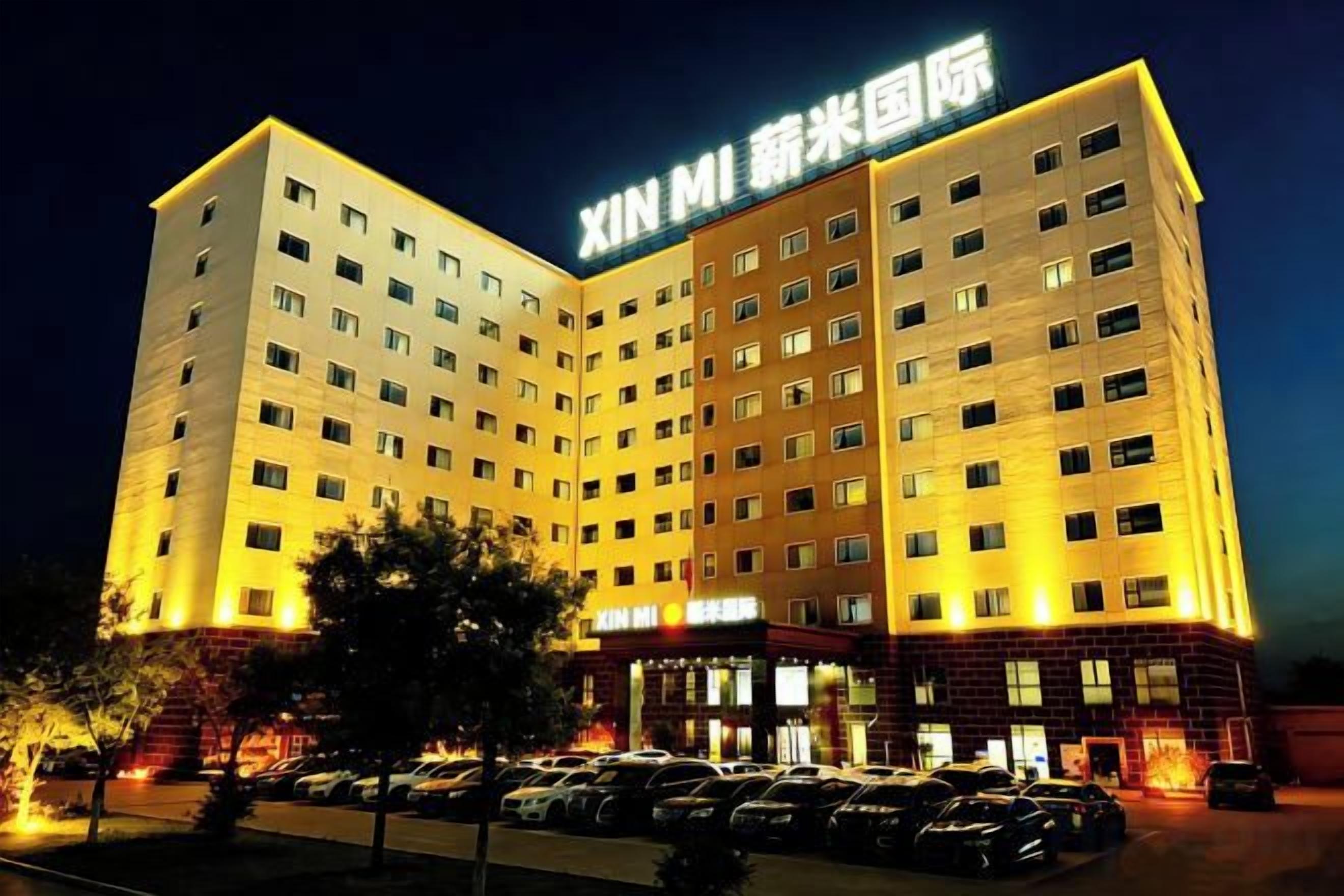 A multi-story hotel with a prominent signage, a parking lot with several cars, and a well-lit facade.