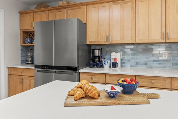 A kitchen with wooden cabinets, a stainless steel refrigerator, a coffee maker, and a bowl of fruit on the counter. - Heated Pool-Hot Tub-Sauna-Pet Friendly-Steps to Beach (Saint Augustine)