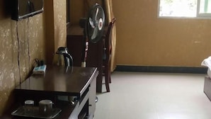 A room with a wooden table, a small fan, a kettle, and a window with curtains. - Bohai Far East Hotel (Menghai)