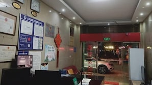 A reception area with a desk, chairs, and a television. There are certificates and documents on the wall, and a car is visible through the glass door. - Bohai Far East Hotel (Menghai)
