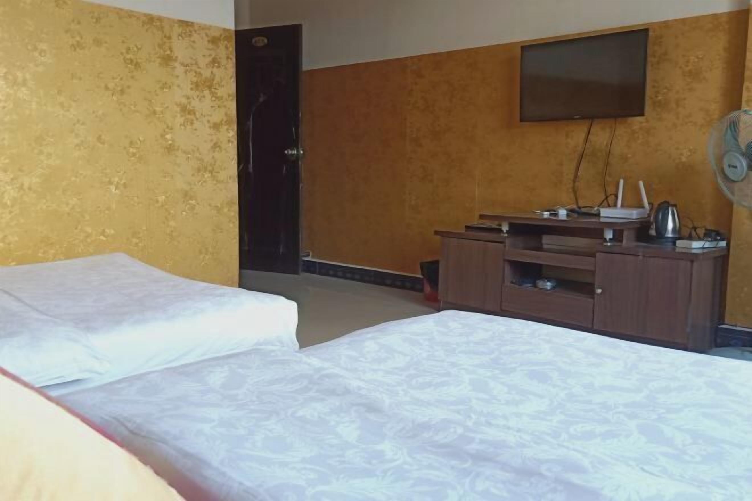 Quarto de hotel com duas camas, uma televisão, uma escrivaninha e um ventoinha, e uma porta.