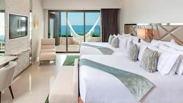 Habitación de hotel con una cama grande, una silla, un escritorio y vista al océano a través de un ventanal.