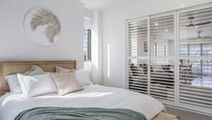 Ein Schlafzimmer mit einem großen Bett, einem Kopfteil und Blick durch eine Schiebetür auf einen Außenbereich.