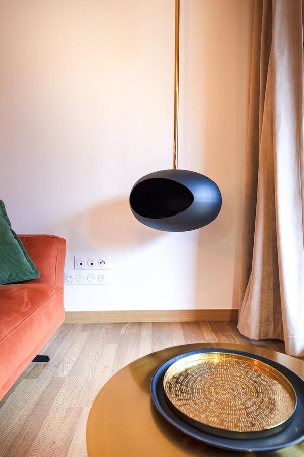 A modern living room with a black hanging lamp, a wooden floor, a red sofa, and a woven side table.